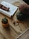 A cozy crafting setup featuring a rolled magazine, a crocheted doll, some yarn balls in brown and green, a crochet hook, and a small potted cactus on a table with a textured cloth.