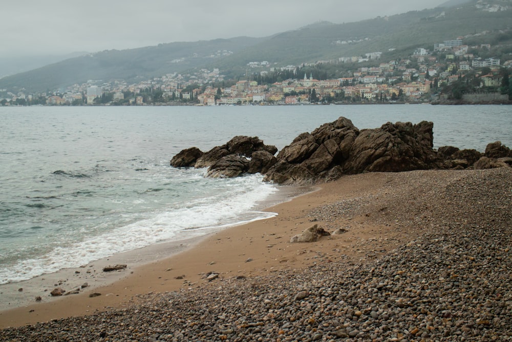 uma praia rochosa com um corpo de água e uma cidade ao fundo