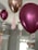 Several metallic balloons in shades of pink and gold are floating indoors with ribbons attached at the bottom. Soft lighting highlights their shiny surfaces and the surrounding neutral-colored walls offer a subtle backdrop.