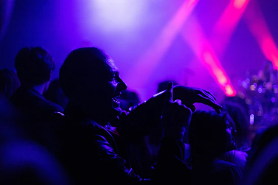 A vibrant crowd enjoying a live music performance under magenta and black festival lights.