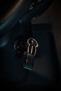 A key with a black leather strap and a metal clasp, featuring the brand name 'Nissan'. It is inserted into the ignition of a car, which is part of a dark interior, including sections of the steering wheel and dashboard.