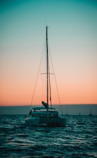 A serene sailboat gliding on calm blue waters at sunset.