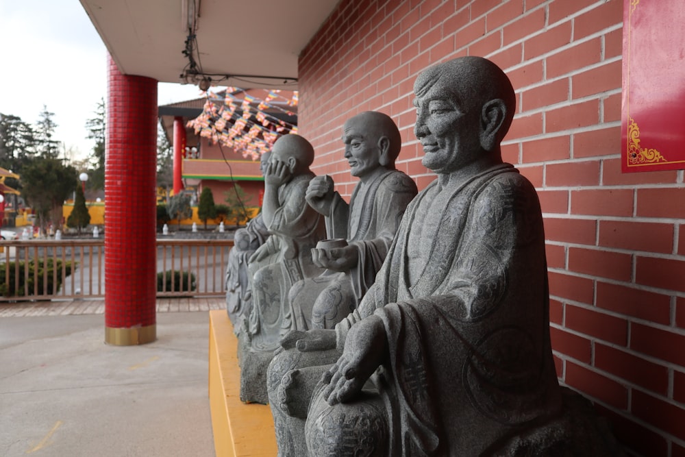 a group of buddha statues sitting next to a red brick wall