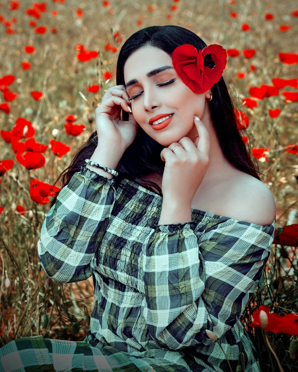 a woman sitting in a field of red flowers