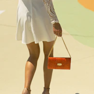 A soft yellow sundress paired with white sneakers and a peach-colored handbag on a sunny street.