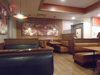 A cozy restaurant interior featuring brown leather booth seating and wood flooring. A mural with various food images decorates the wall, and warm lighting creates an inviting atmosphere.