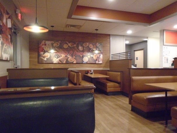 A cozy restaurant interior featuring brown leather booth seating and wood flooring. A mural with various food images decorates the wall, and warm lighting creates an inviting atmosphere.