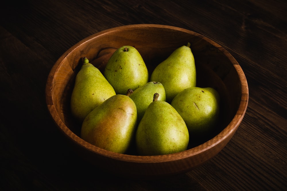 a wooden bowl filled with green pears on top of a wooden table