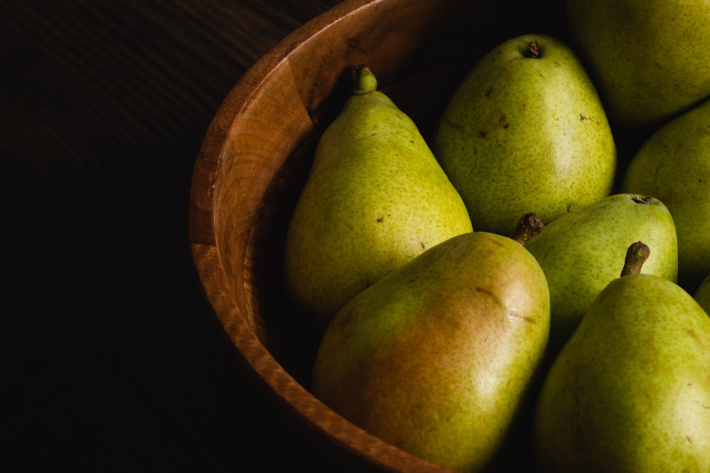 a wooden bowl filled with green pears on top of a table