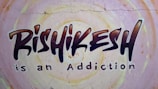 Graffiti-style mural on a wall with the text 'Rishikesh is an Addiction'. The background features circular patterns in pastel colors.
