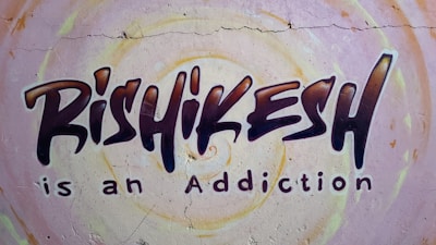 Graffiti-style mural on a wall with the text 'Rishikesh is an Addiction'. The background features circular patterns in pastel colors.