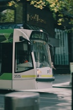 A modern tram moving along a tree-lined urban street on a sunny day.