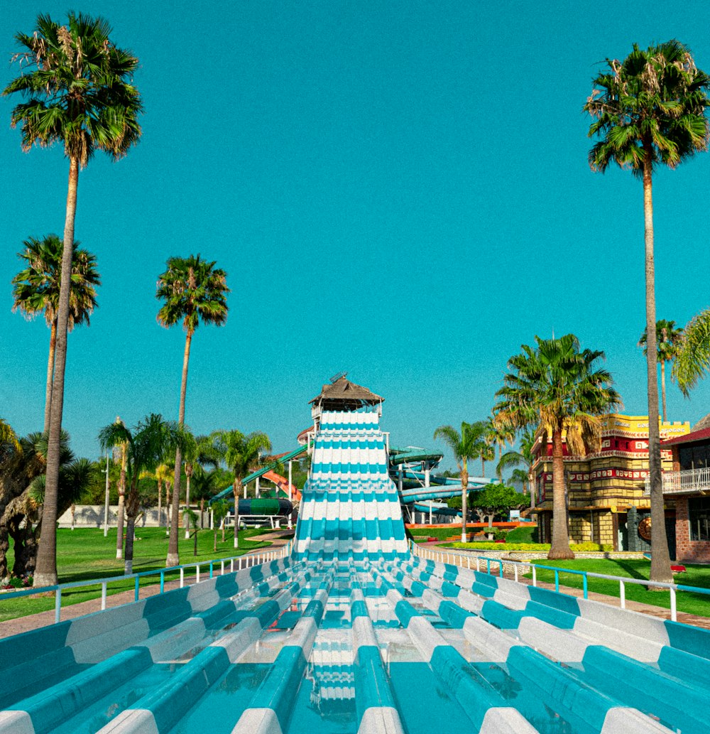 a blue and white water slide in the middle of palm trees