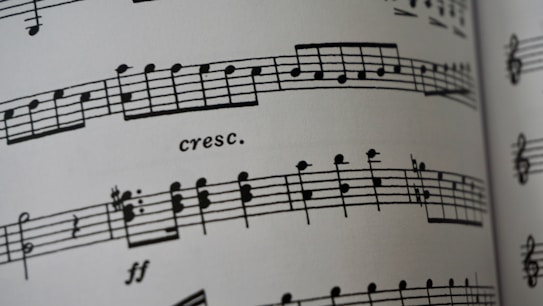 A close-up of a sheet of printed music featuring musical notes and symbols on a staff line. The term 'cresc.' appears, indicating a crescendo. The paper appears to curve slightly, suggesting the image captures a part of an open book.