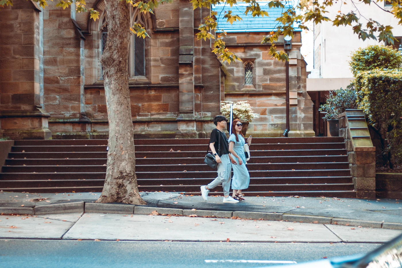 A couple walking past brick steps on a tree-lined street
