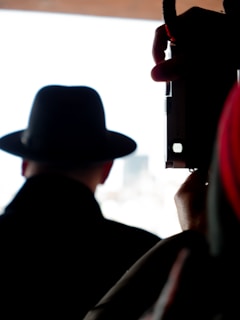 A silhouette of a person wearing a fedora hat, sitting in front of a laptop with encrypted files on screen.