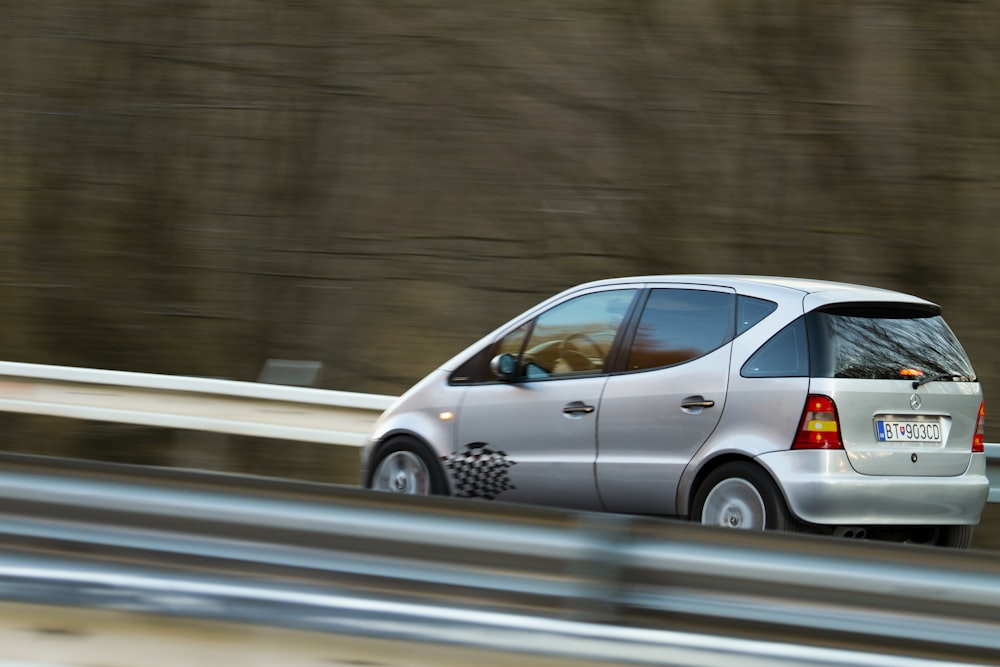 Un coche plateado conduciendo por una carretera junto a un bosque