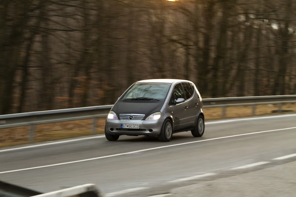 a silver van driving down a road next to a forest