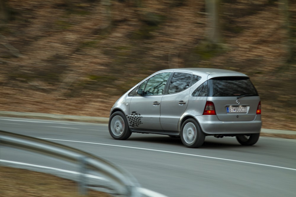 a silver car driving down a road next to a forest