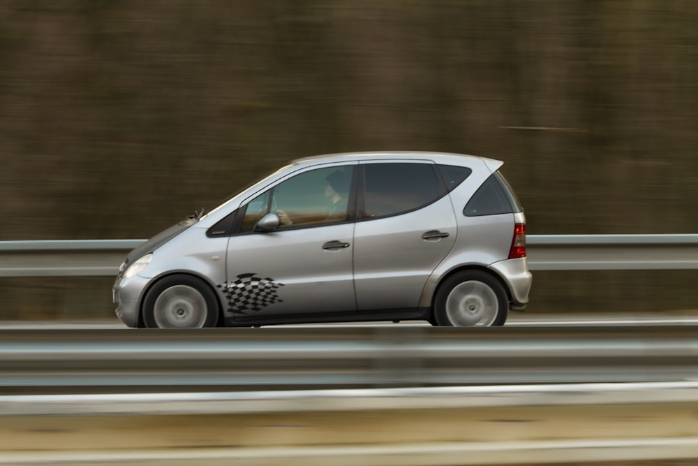 a silver car driving down a highway next to a forest