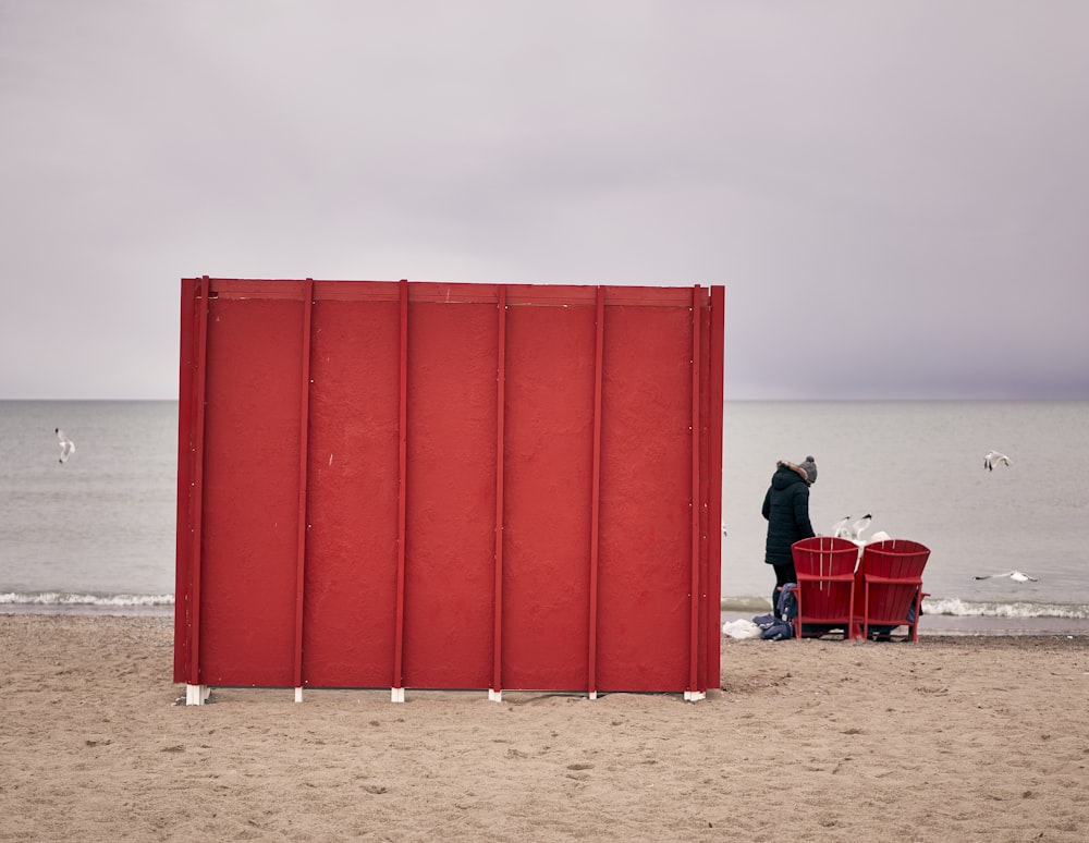 um homem de pé ao lado de uma caixa vermelha em uma praia
