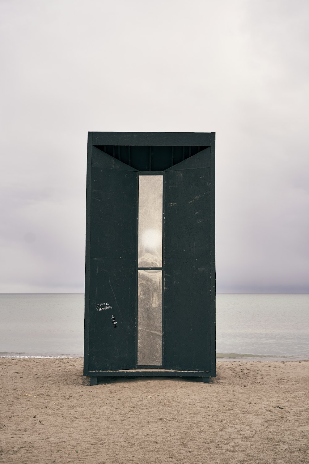 a black outhouse sitting on top of a sandy beach