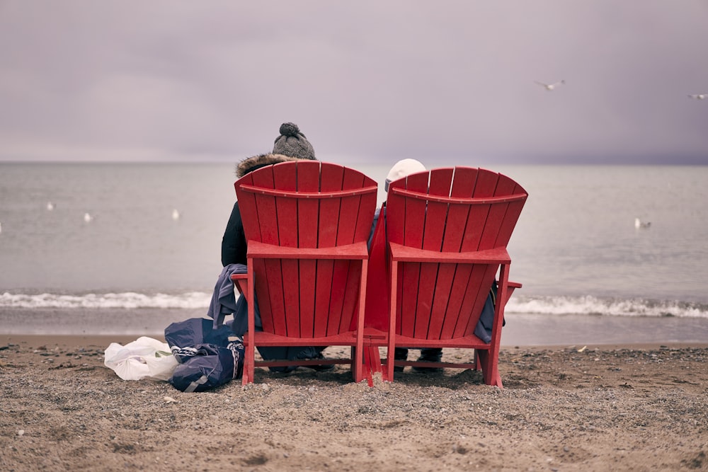 a couple of red chairs sitting on top of a sandy beach