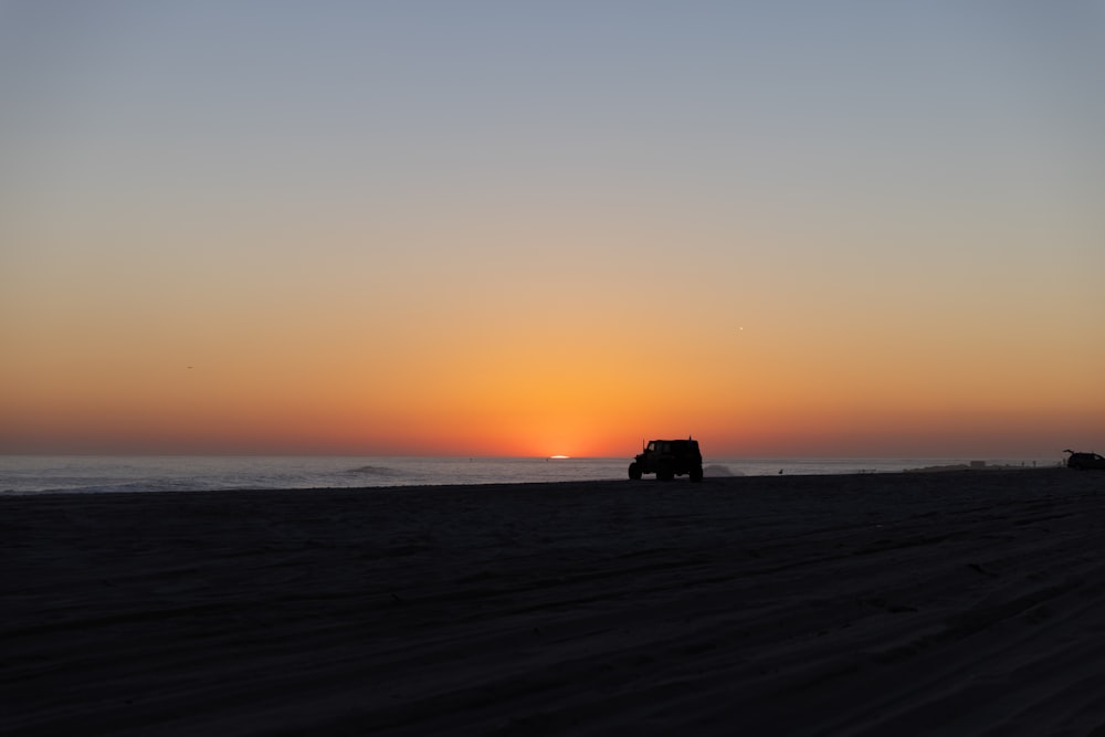 a truck driving down a beach at sunset