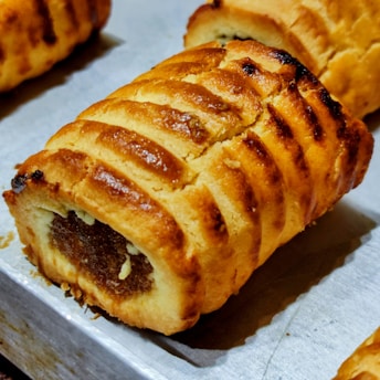 Golden-brown pastries with a flaky crust are arranged on a baking tray. The pastries have a filled center and a scored top, highlighting their texture.