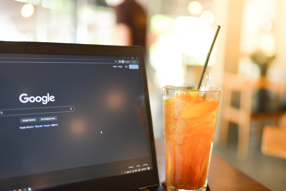 un vaso de jugo de naranja junto a una computadora portátil