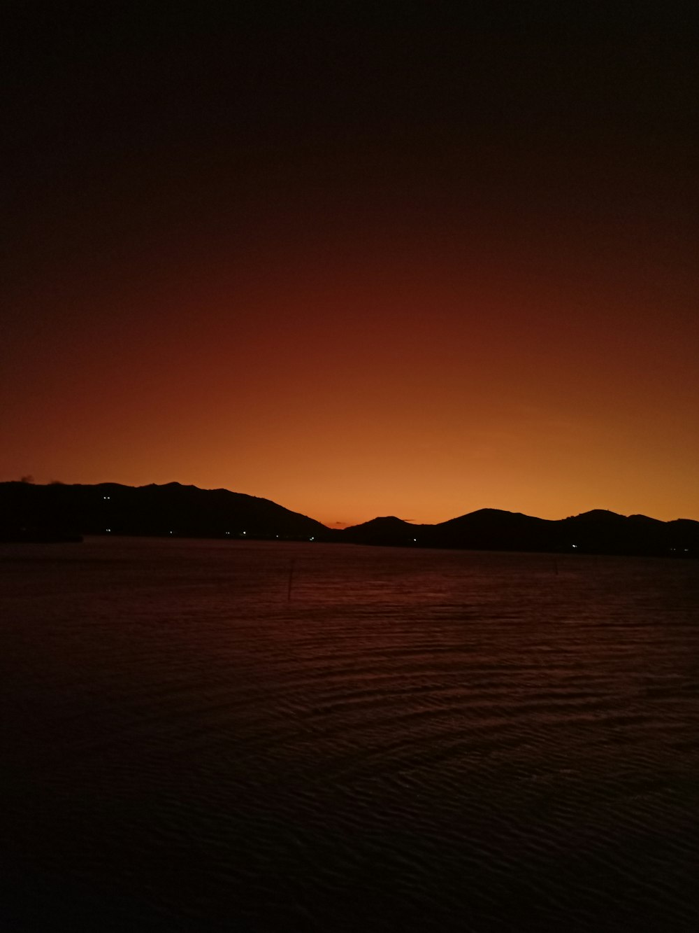 山を背景にした水域に沈む夕日