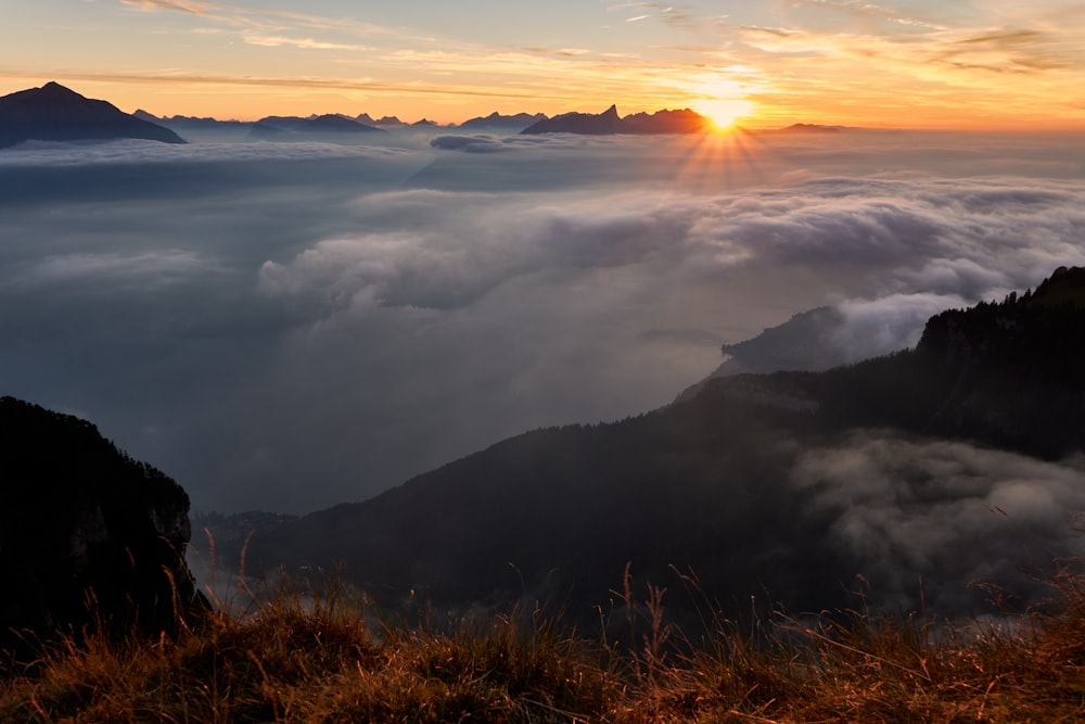 the sun is setting over the mountains and clouds