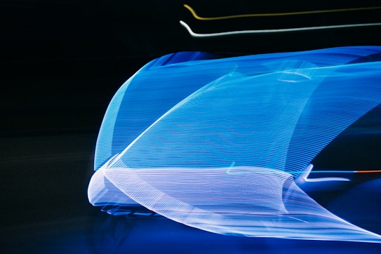 A dynamic display of flowing blue light streaks against a dark background, creating a sense of motion and speed. The lights form abstract patterns with lines and curves, offering a futuristic and vibrant aesthetic.