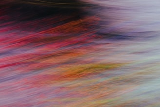 Abstract motion blur featuring a blend of vibrant colors including reds, oranges, purples, and yellows, creating a dynamic, fluid visual effect.