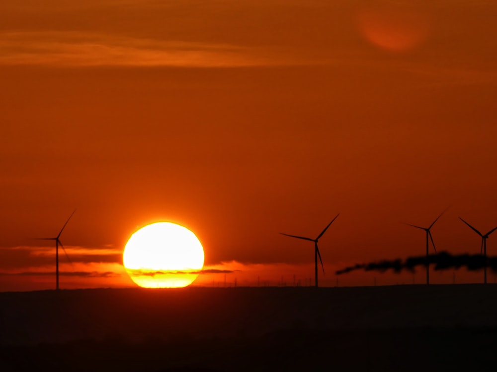 the sun is setting over a field of wind turbines