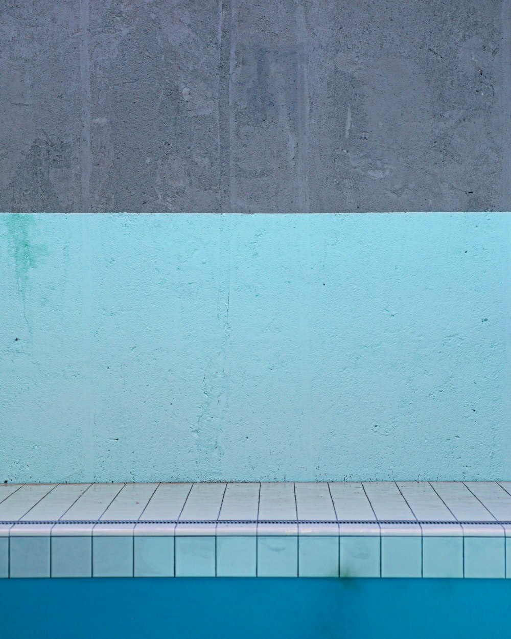 an empty swimming pool with a blue wall and tiled floor