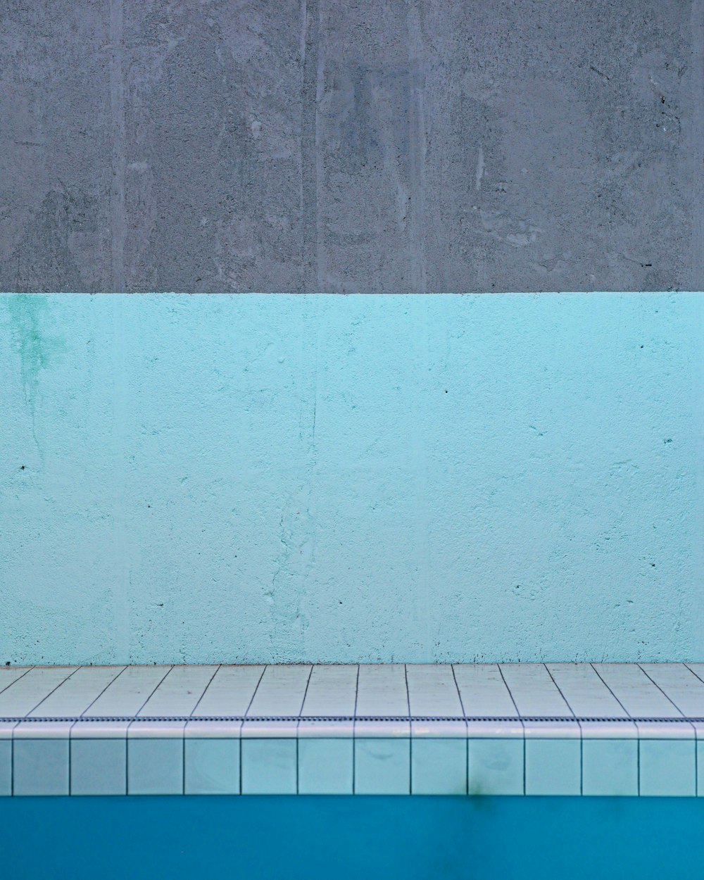 une piscine vide avec un mur bleu et un sol carrelé