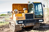 A large yellow Morooka tracked vehicle is positioned on a muddy construction site. It features a spacious cabin with large windows and is equipped with lights on top. There is earth and construction fencing in the background, indicating an active construction area.