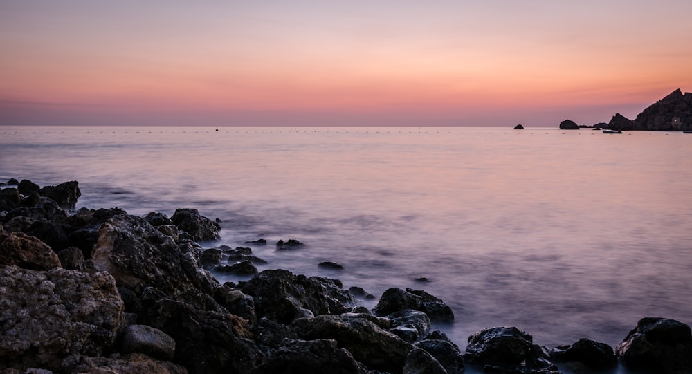 a rocky beach at sunset with a boat in the distance