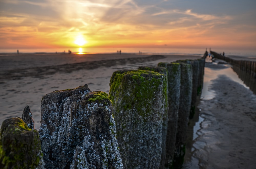 the sun is setting over a beach with a wooden fence