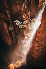 Sunlight filtering through tall canyon walls as a group crosses a rocky riverbed.