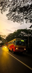 A bright yellow bus driving along a tree-lined city street during sunset.