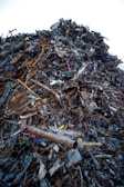 A large heap of assorted scrap metal and debris, including rusted pipes, wires, metal sheets, and various other discarded items, forming a significant pile. The background is a clear sky.