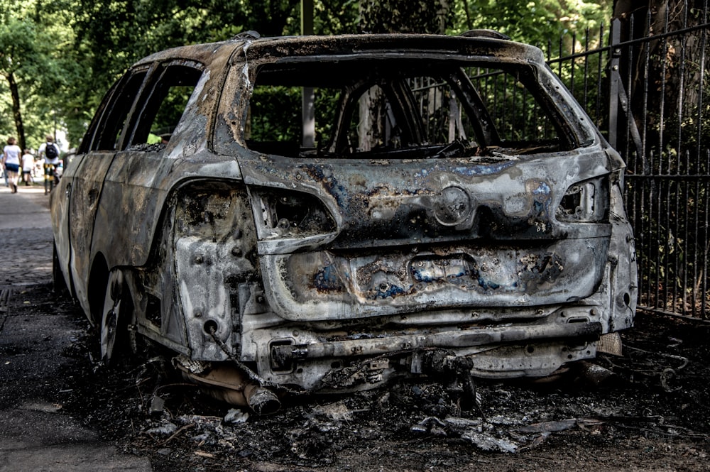 a burnt out car parked in front of a fence