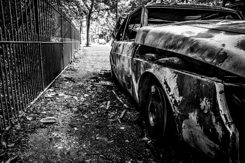 an old rusty car parked in front of a fence