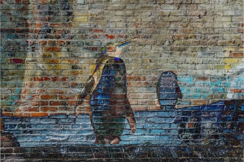 A mural on a brick wall depicts a penguin walking alongside a body of water. The background consists of abstract and blurred images creating an urban and artistic vibe.