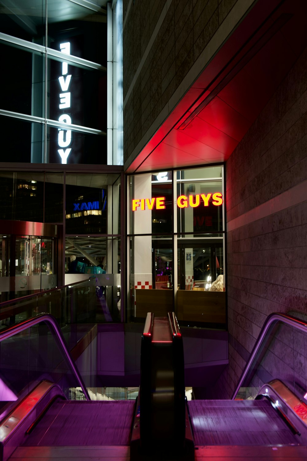 an escalator in front of a building with a neon sign