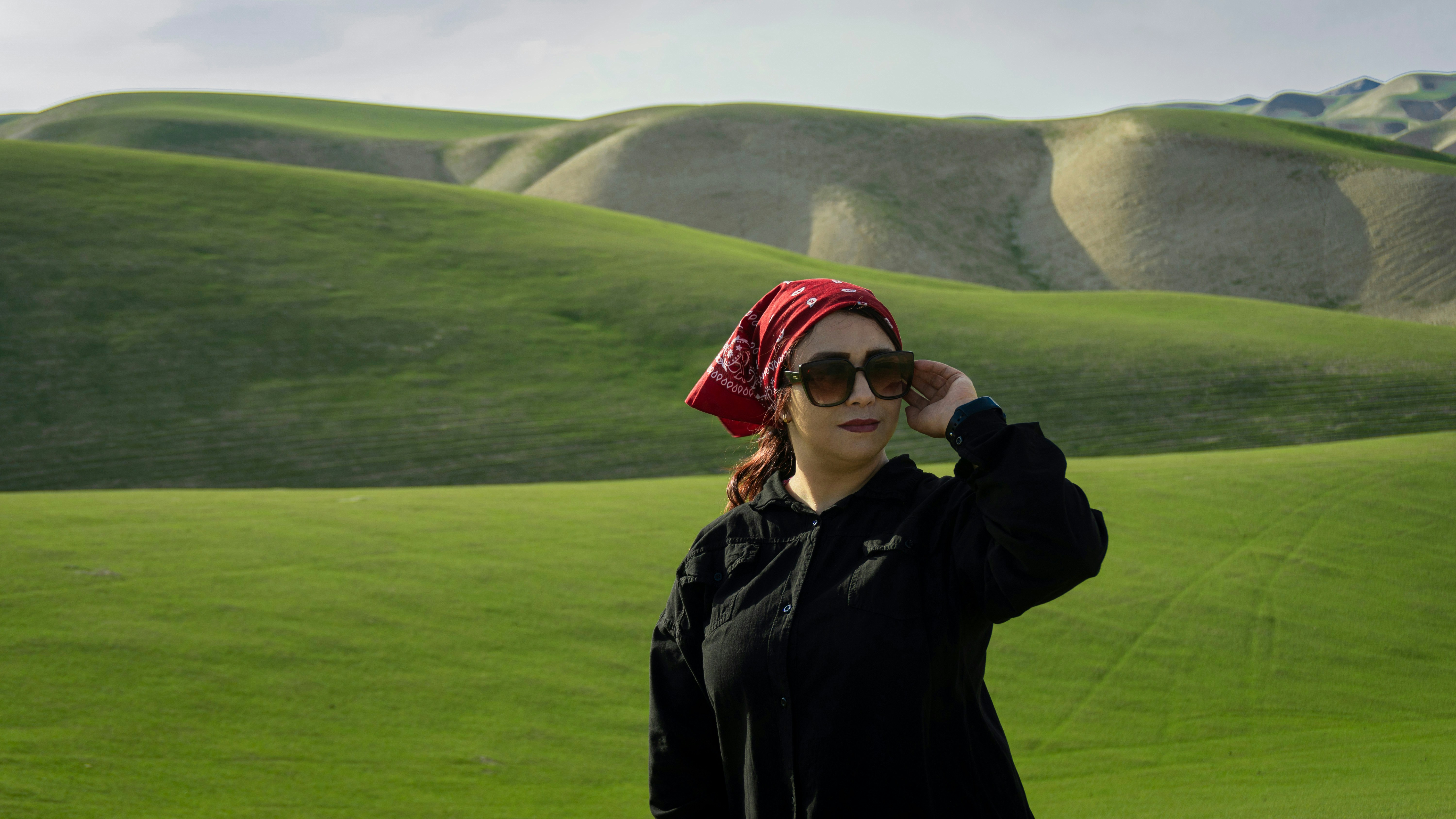 a woman wearing sunglasses and a red bandana stands in a green field