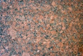 A detailed, intricate pattern of speckled granite stone with a mix of pinkish-brown and dark gray hues, featuring a naturally textured surface.