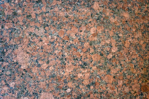 A detailed, intricate pattern of speckled granite stone with a mix of pinkish-brown and dark gray hues, featuring a naturally textured surface.